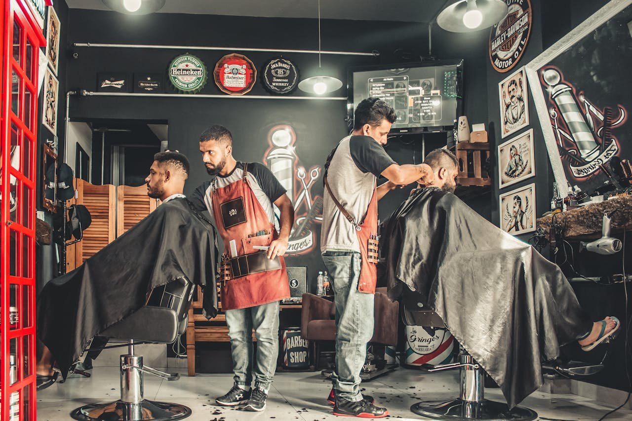 Servicios. A bustling barbershop with two men getting haircuts, showcasing a vibrant barber environment.